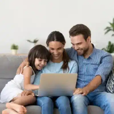 Choose tuckahoe creek dental for your family 3 Family sitting on a couch together working on a laptop, representing your family dentist